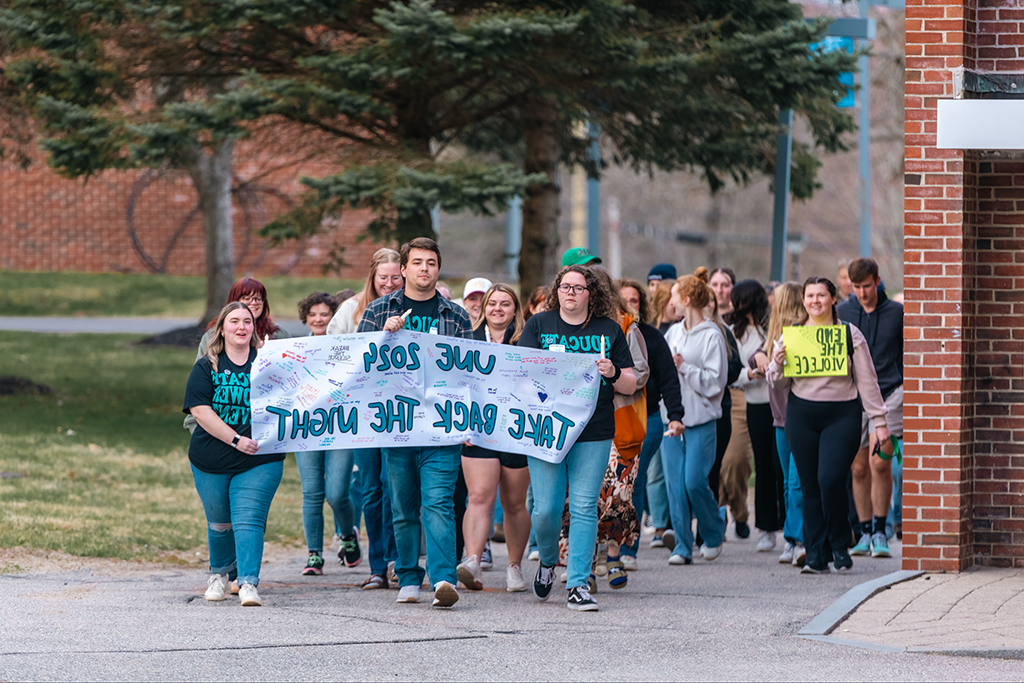 一群学生在校园里游行，举着一个标语，上面写着“全球网络赌博平台2024年夺回夜晚”。